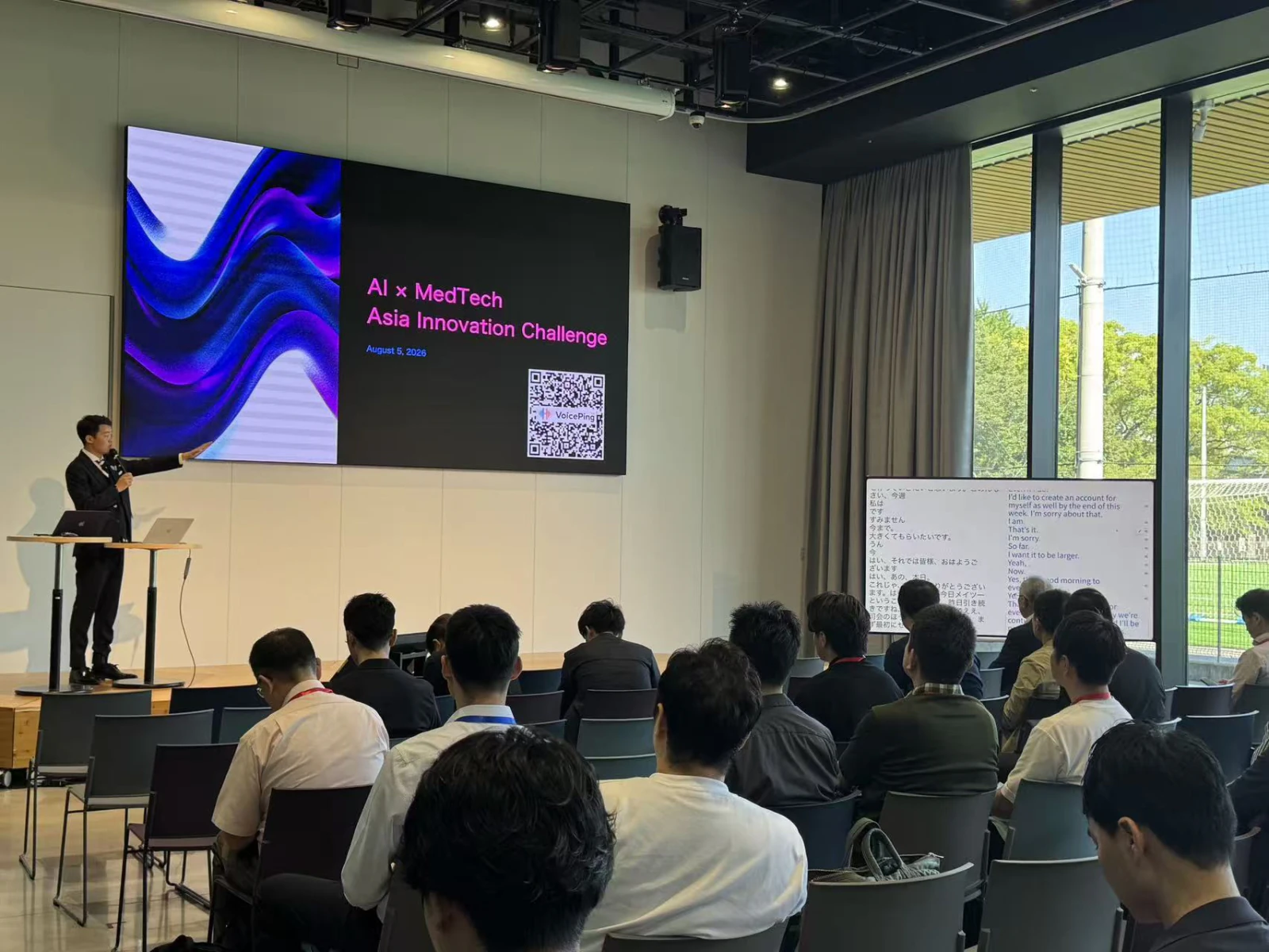STATION Ai现场介绍AI×MedTech的演讲者；主屏幕显示活动名称和VoicePing二维码，舞台旁显示日英字幕。
