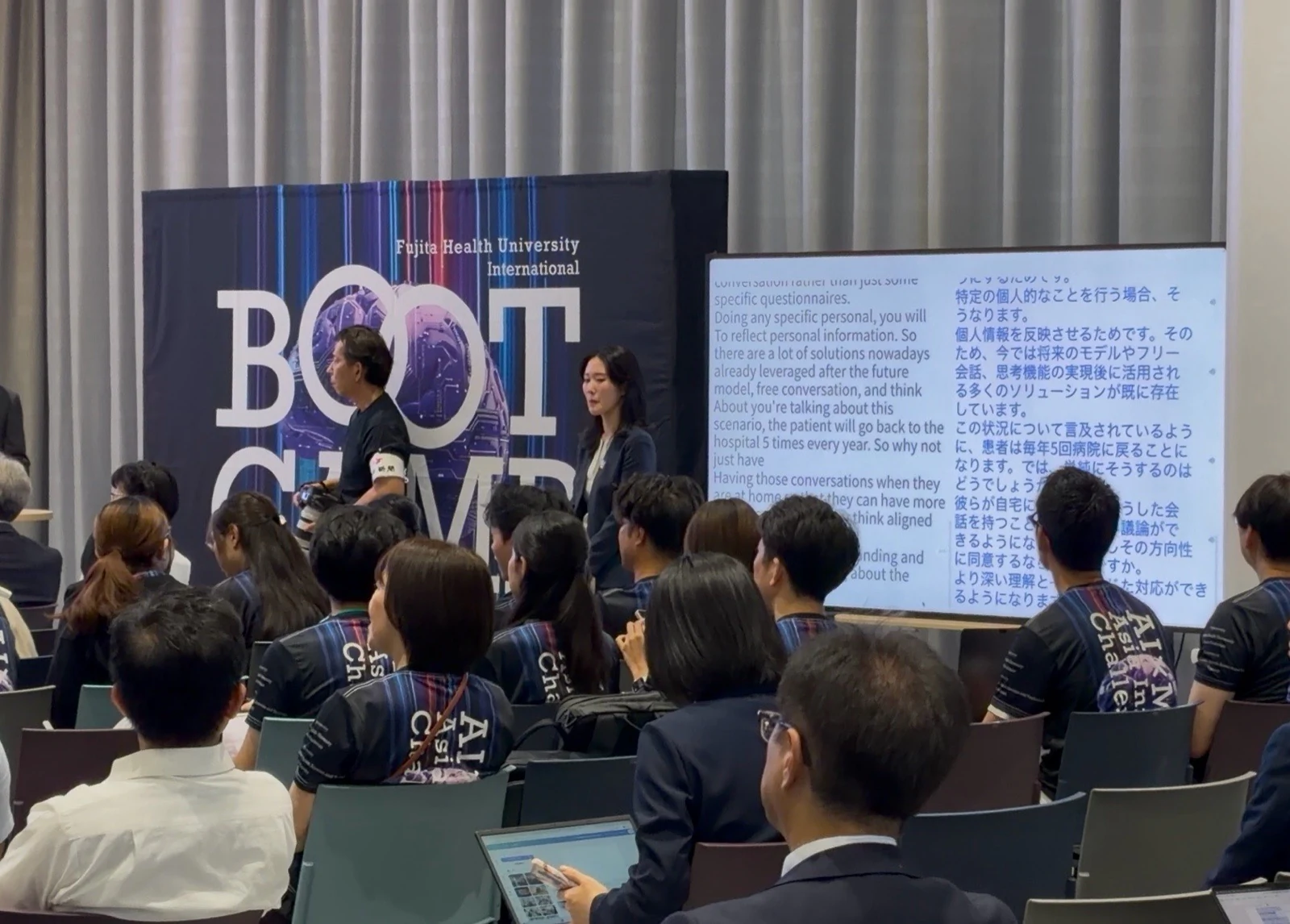 An AI×MedTech speaker beside a large display showing English and Japanese live captions to the audience.