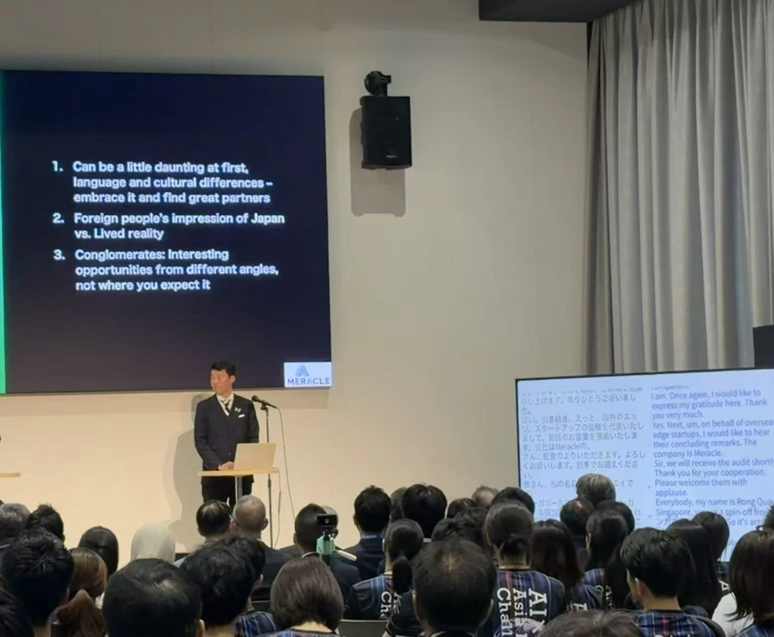 STATION Ai现场，一位AI×MedTech演讲者在日英实时字幕屏幕旁进行演讲。