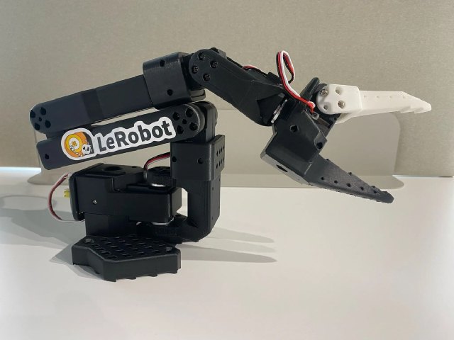 SO-101 follower arm with black printed links, exposed wiring, and a parallel-jaw gripper.